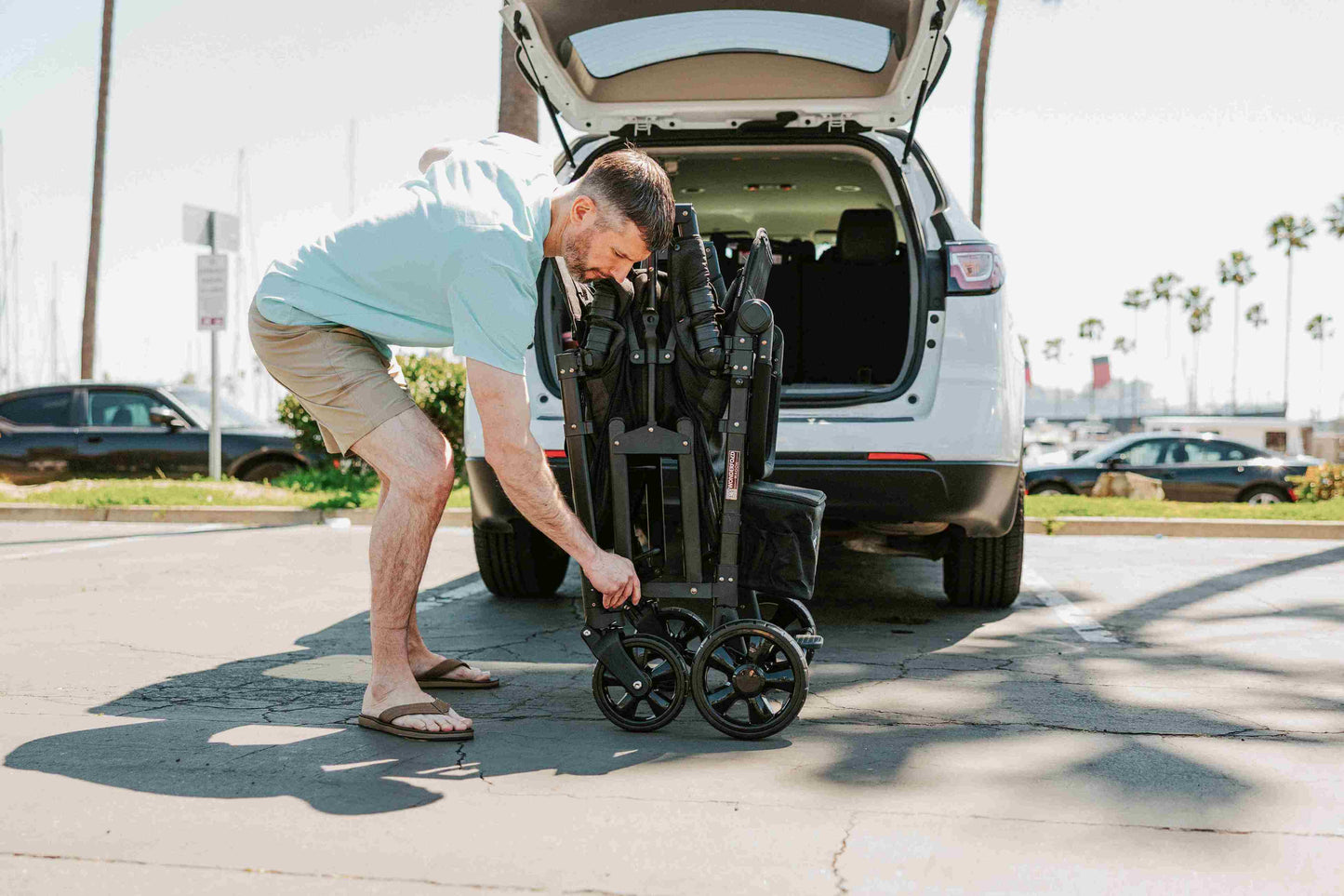 W4 Elite Quad Stroller Wagon - Lifestyle Image of Man Folding W4 Elite Quad Stroller Wagon Black