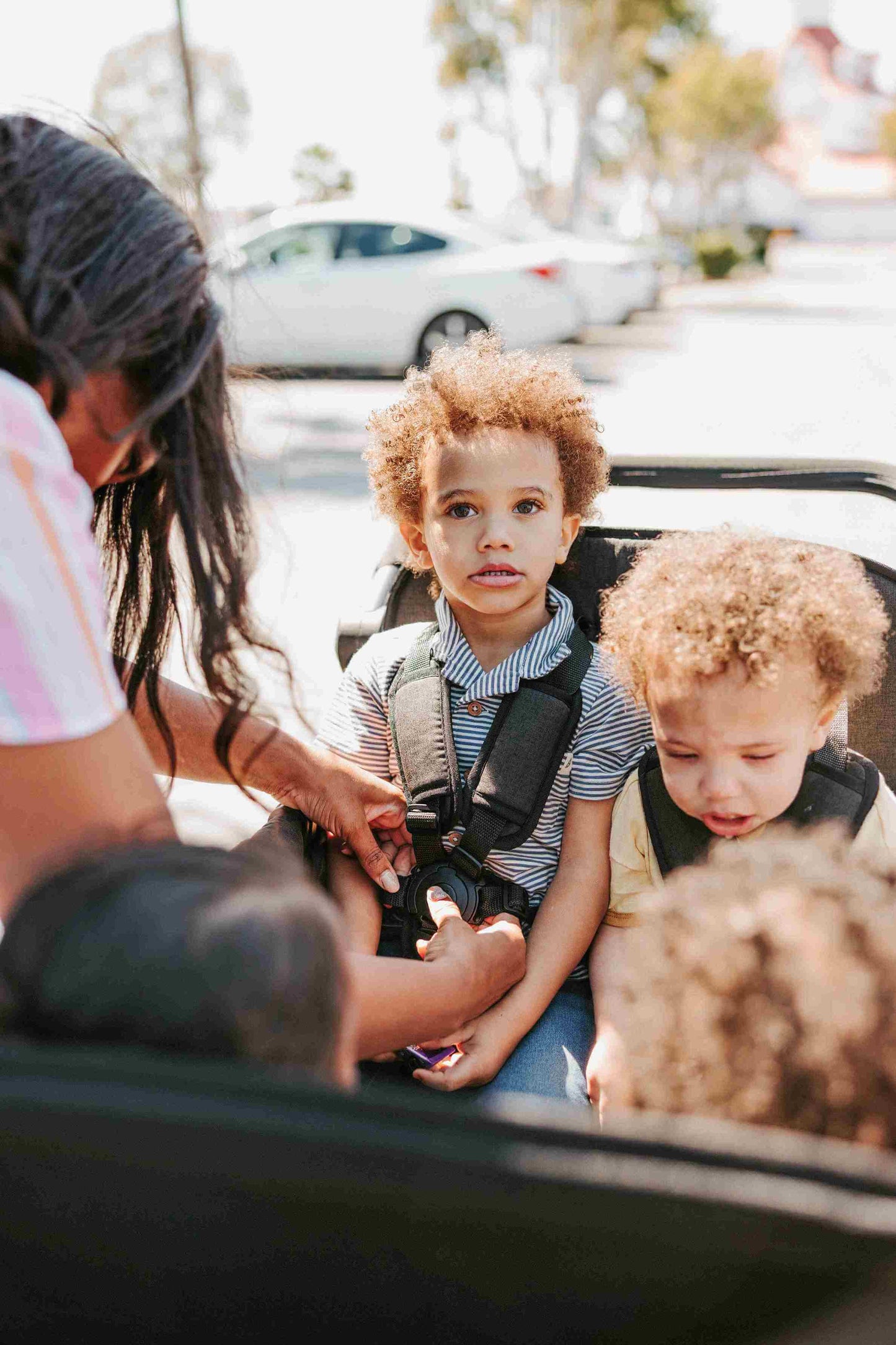 W4 Elite Quad Stroller Wagon - Zoomed Lifestyle Image of Mother Helping Baby with Harness of W4 Elite Quad Stroller Wagon Black