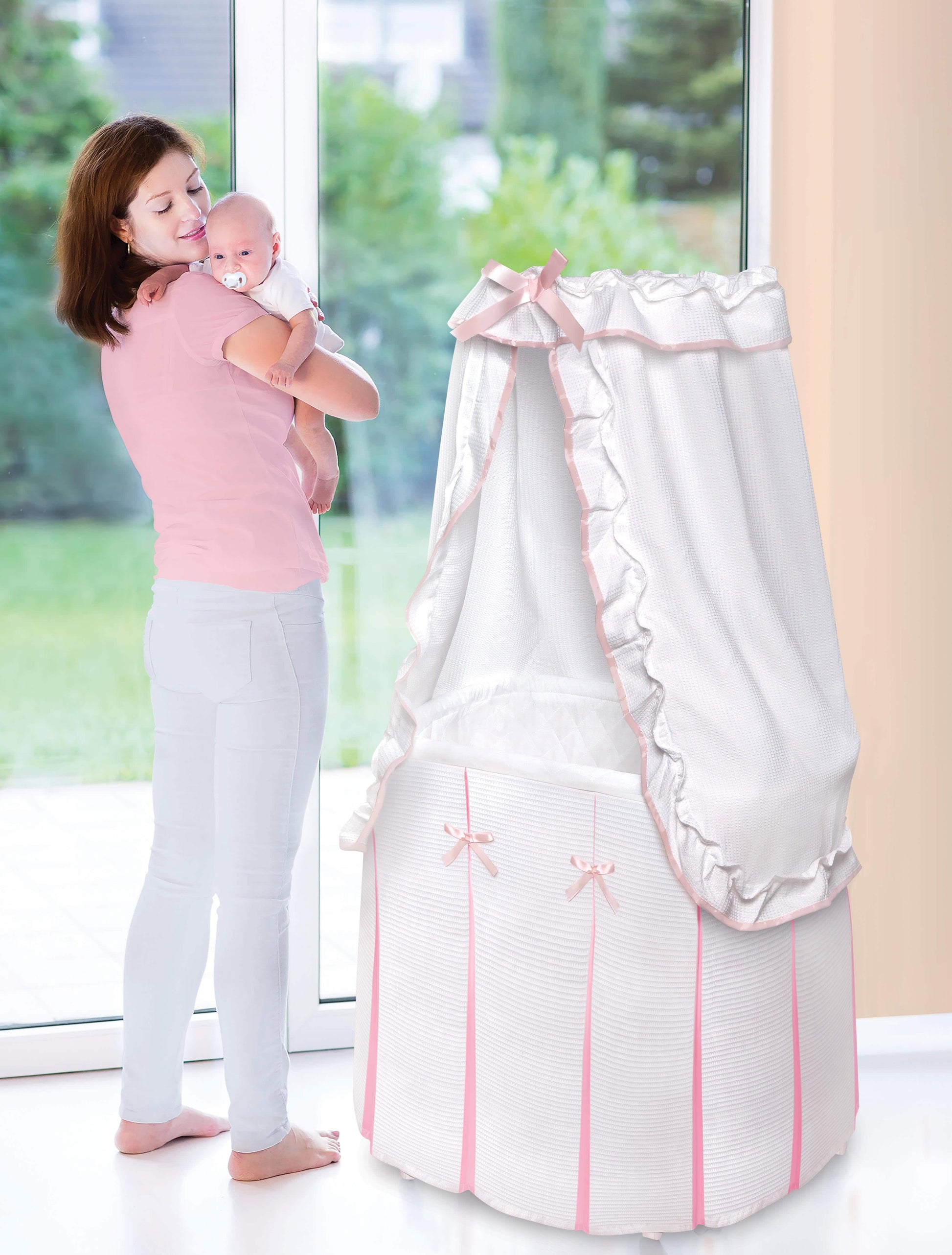 Majesty Baby Bassinet with Canopy - Lifestyle Image of Mother Holding Baby Beside Majesty Baby Bassinet with Canopy Pink