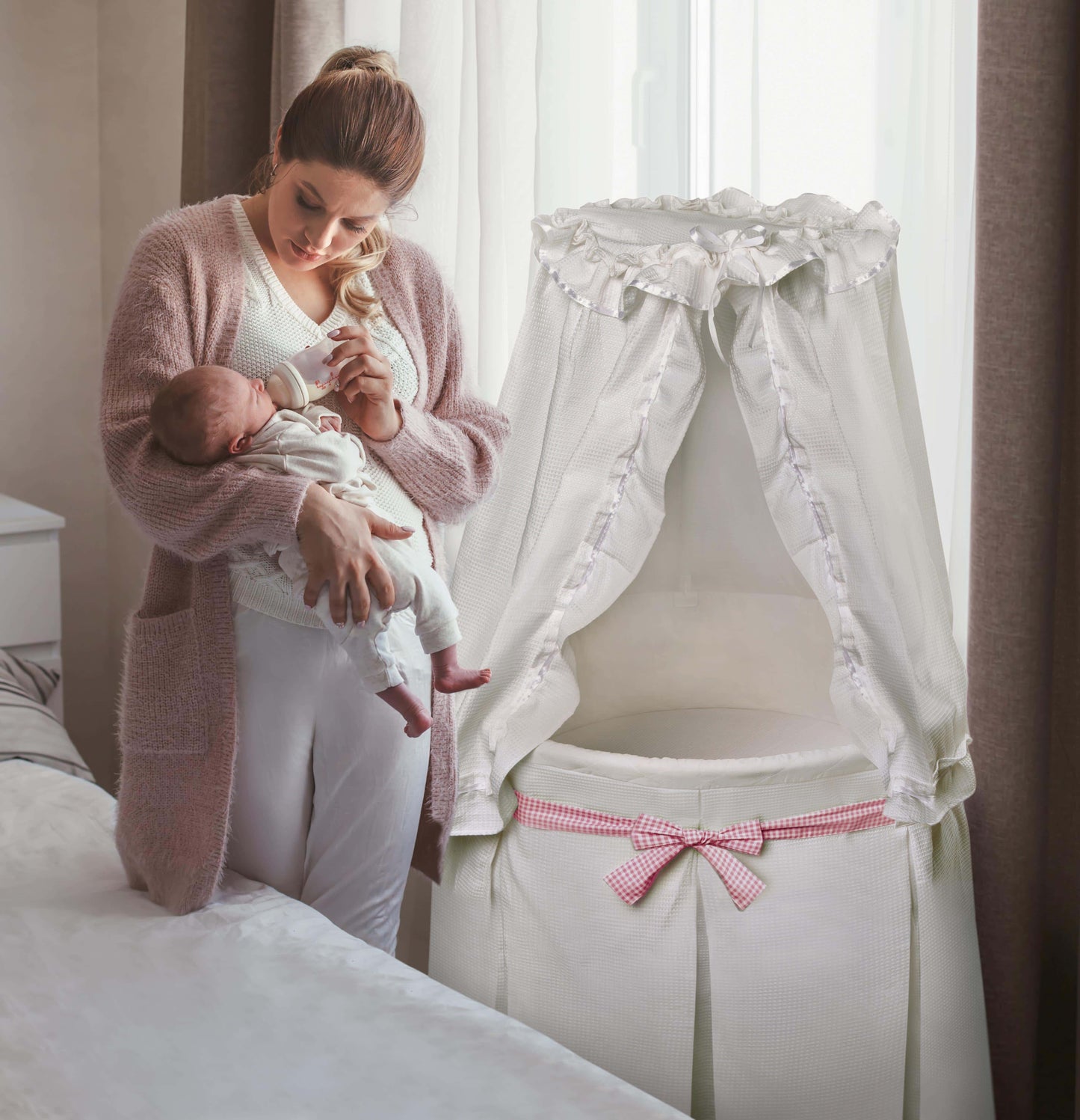 Empress Round Baby Bassinet with Canopy - Lifestyle Image of Mother Holding Baby Beside Empress Round Baby Bassinet with Canopy White