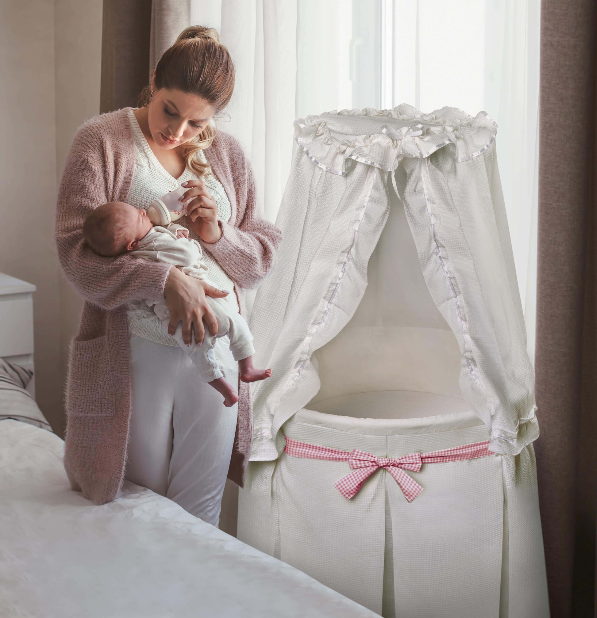 Empress Round Baby Bassinet with Canopy - Lifestyle Image of Mother Holding Baby Beside Empress Round Baby Bassinet with Canopy White