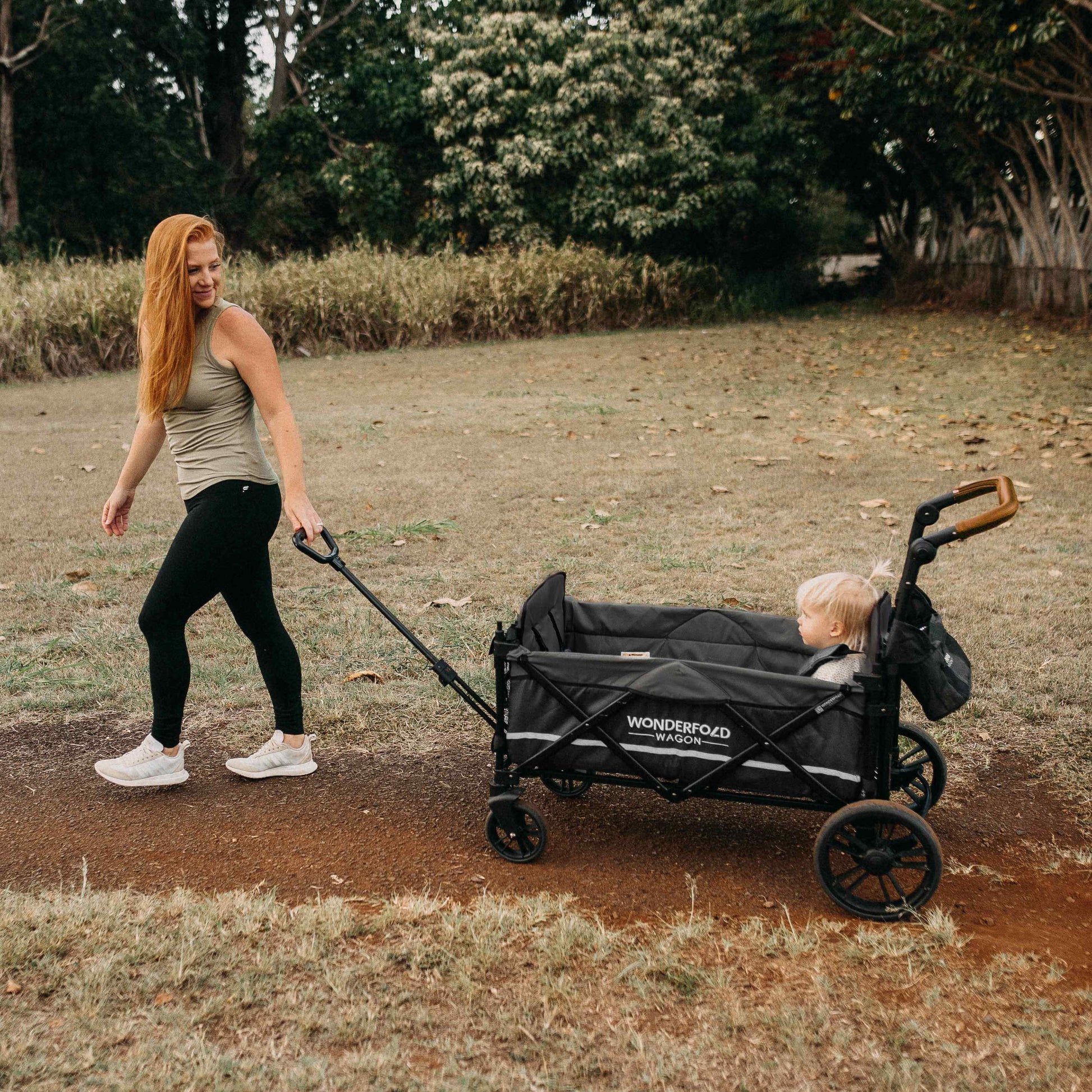 X2 Double Stroller Wagon - Lifestyle Image of Mother Holding Pull Handle of X2 Double Stroller Wagon with Baby Inside Wagon Black