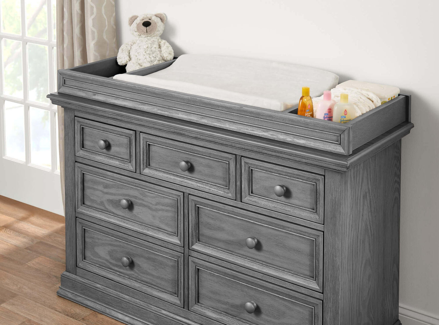 Glenbrook Changing Topper - Lifestyle Image Inclined Side View of Glenbrook Changing Topper Gray on Top of Double Drawer Dresser