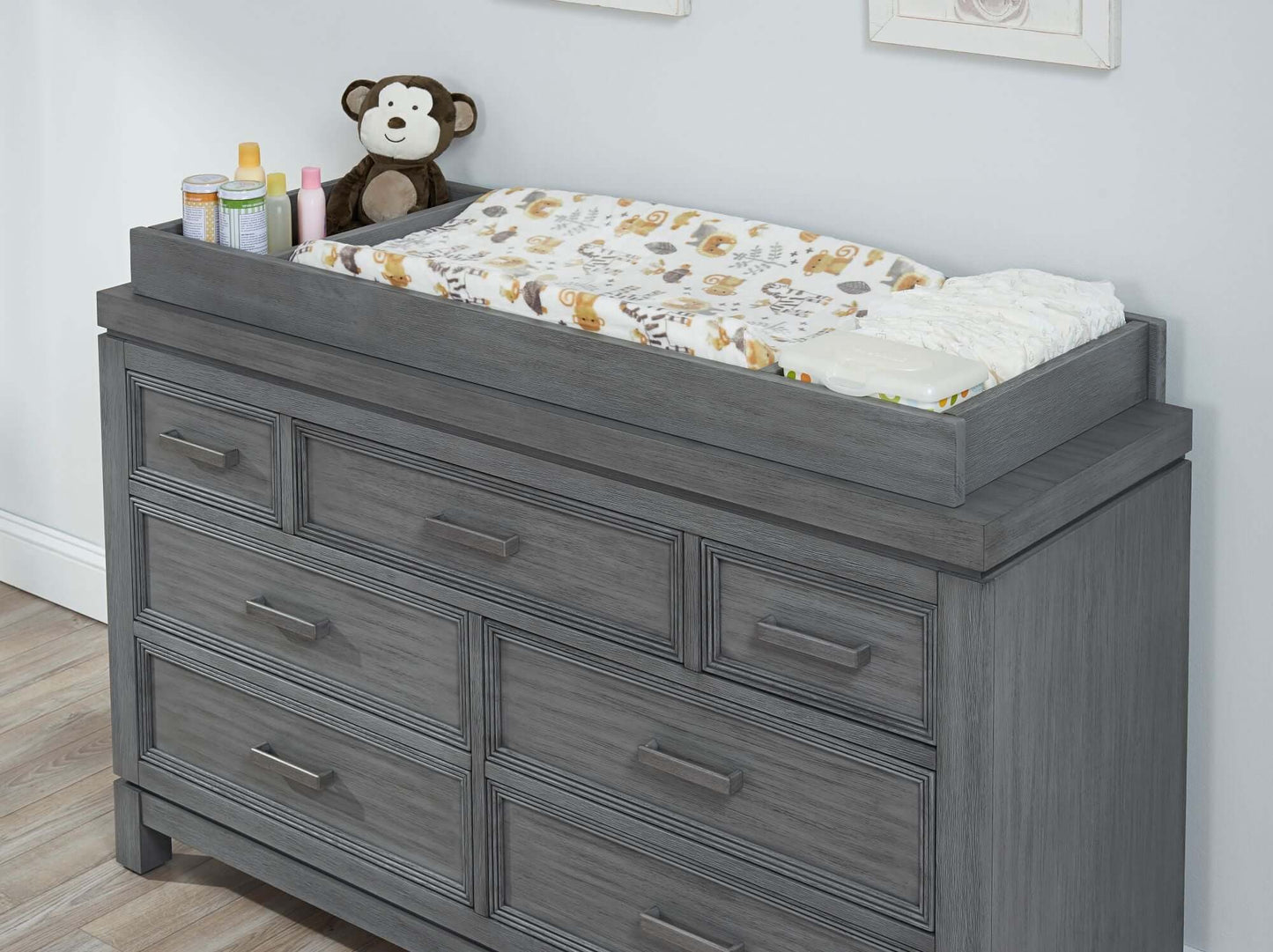Manchester Changing Topper - Lifestyle Image Inclined Side View of Manchester Changing Topper Rustic Gray on Top of 6 Drawer Dresser