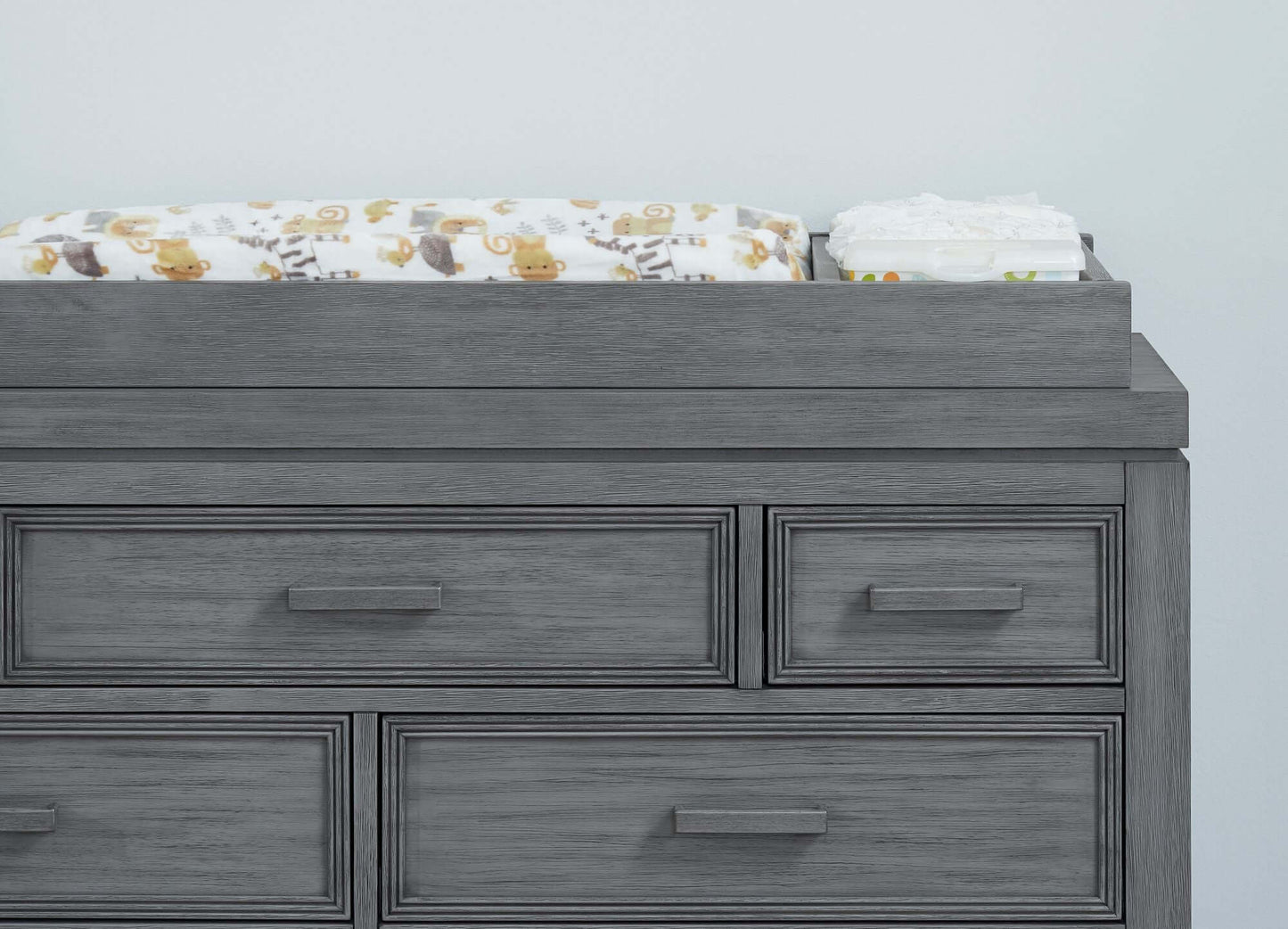 Manchester Changing Topper - Lifestyle Image Front View of Manchester Changing Topper Rustic Gray on Top of 6 Drawer Dresser