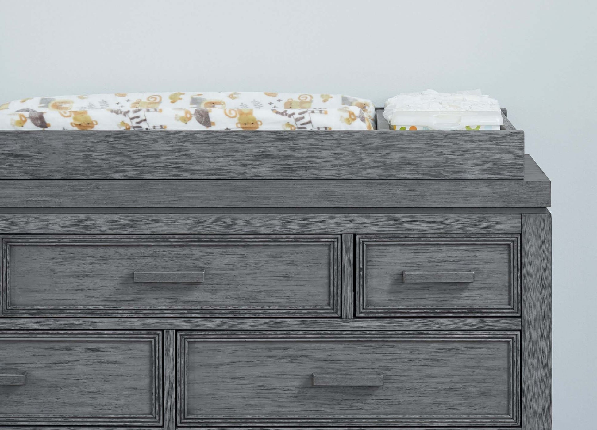 Manchester Changing Topper - Lifestyle Image Front View of Manchester Changing Topper Rustic Gray on Top of 6 Drawer Dresser