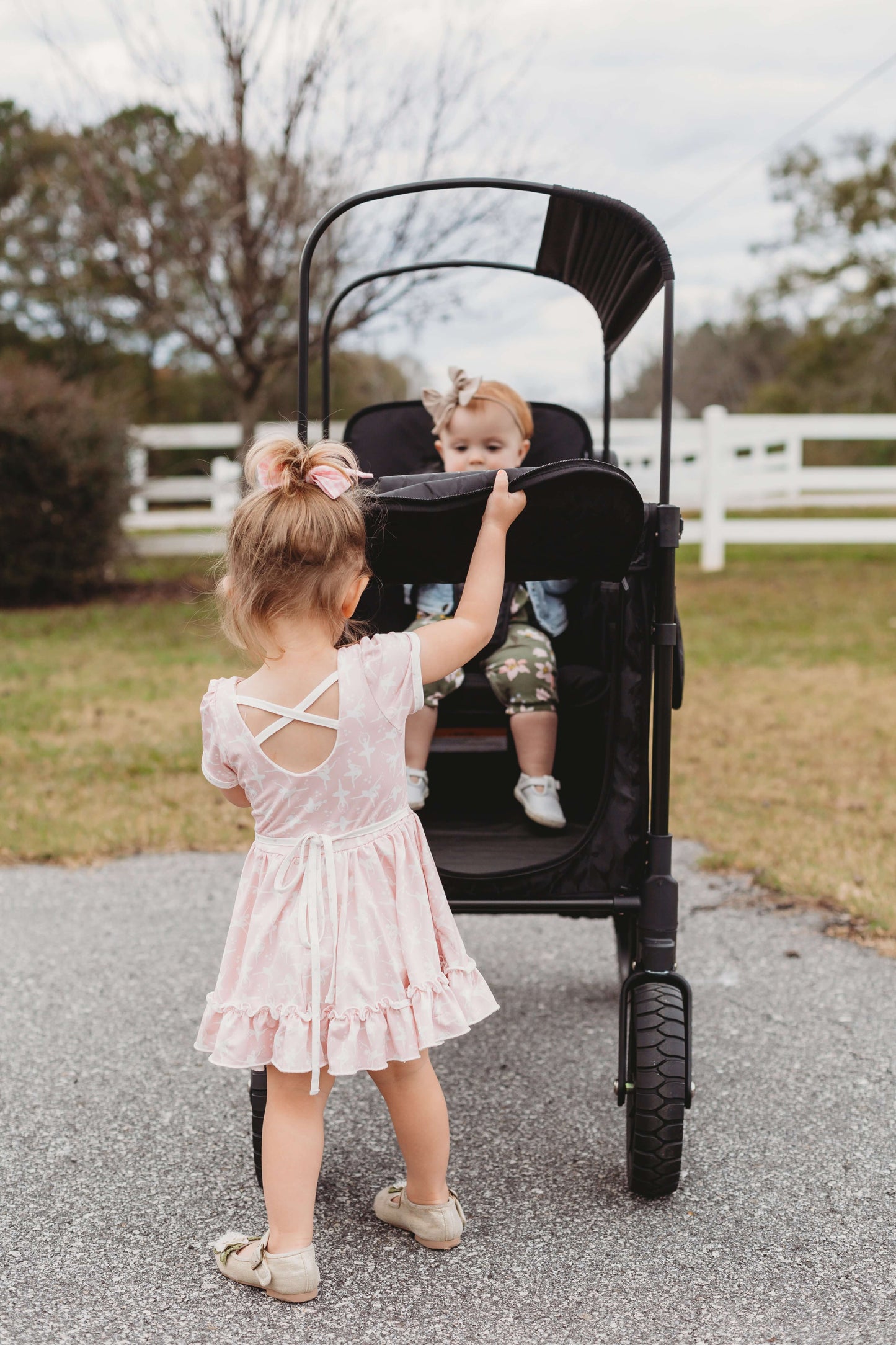 W2 Luxe Double Stroller Wagon - Lifestyle Image Front View of Teenager Helping Toddler To get Out of W2 Luxe Double Stroller Wagon Black