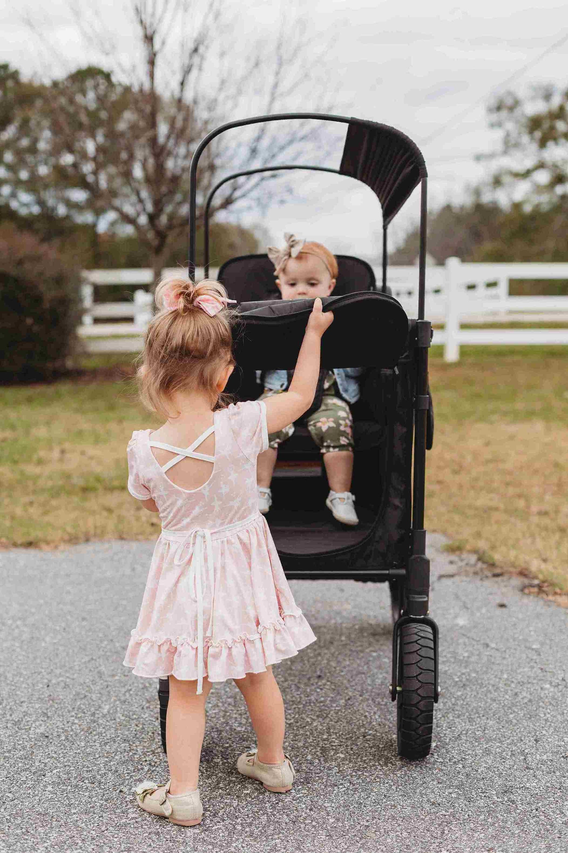 W2 Luxe Double Stroller Wagon - Lifestyle Image Front View of Teenager Helping Toddler To get Out of W2 Luxe Double Stroller Wagon Black