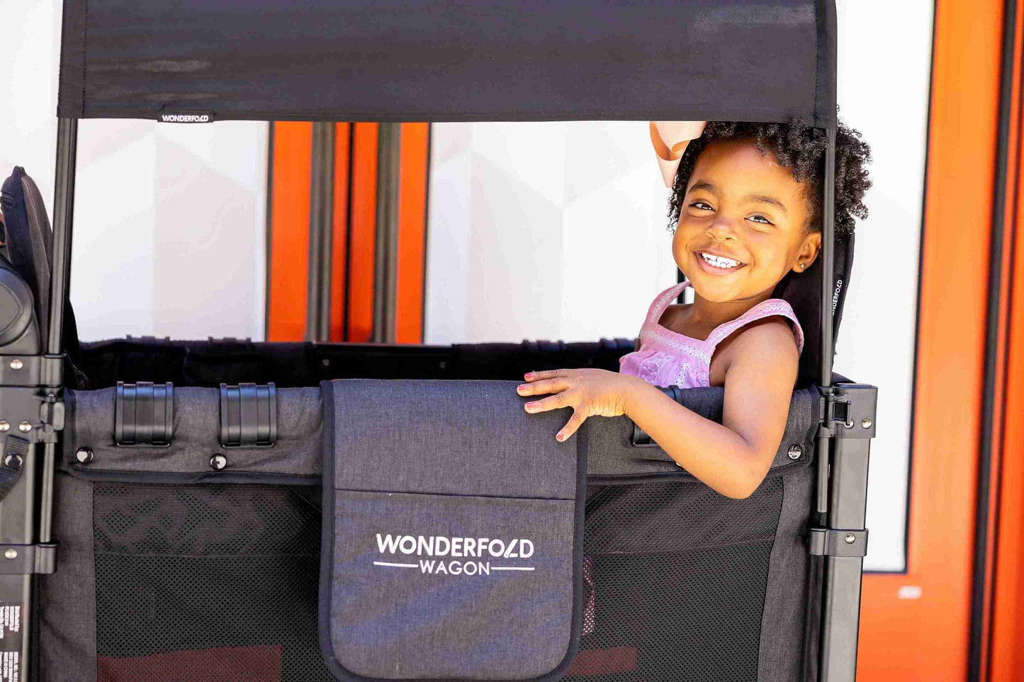 W2 Luxe Double Stroller Wagon - Lifestyle Image Side View of Toddler Peaking From W2 Luxe Double Stroller Wagon Gray