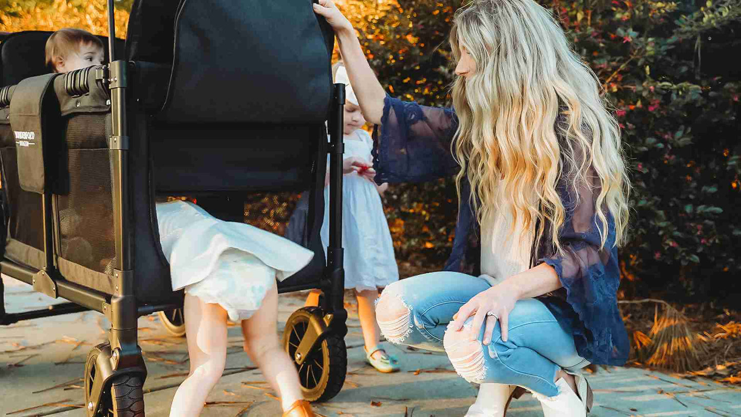 W4 Luxe Quad Stroller Wagon - Lifestyle Image of Mother Helping Toddler to get out of W4 Luxe Quad Stroller Wagon Black