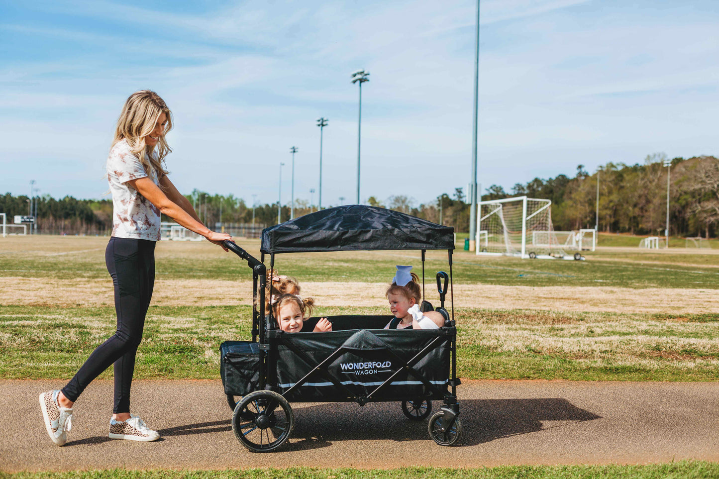 X4 Push + Pull Quad Stroller Wagon - Lifestyle Image Side View of Mother Holding Push Handle of X4 Push + Pull Quad Stroller Wagon Black With Kids Inside
