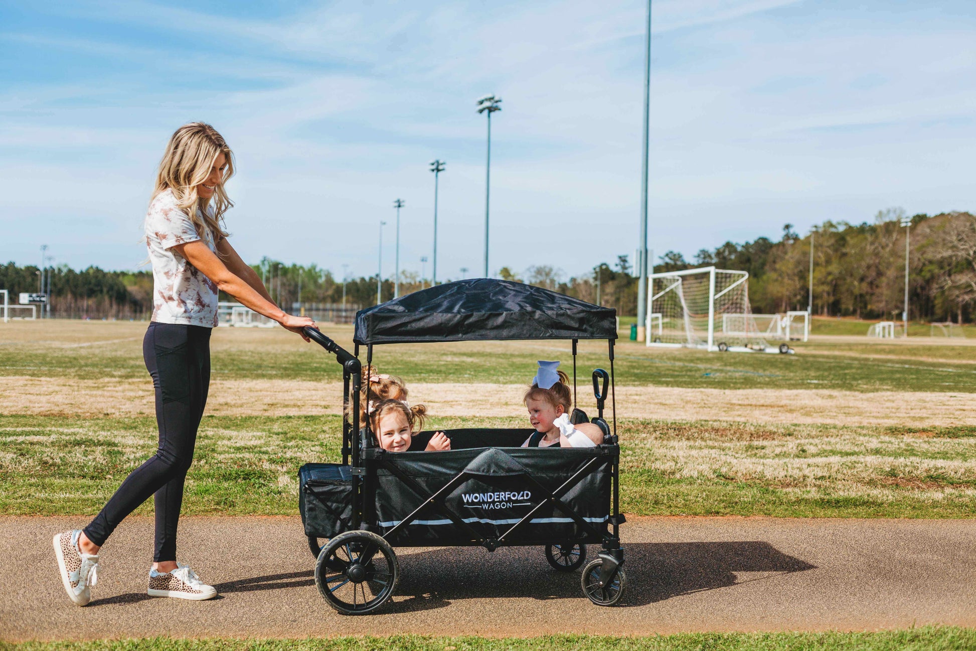X4 Push + Pull Quad Stroller Wagon - Lifestyle Image Side View of Mother Holding Push Handle of X4 Push + Pull Quad Stroller Wagon Black With Kids Inside